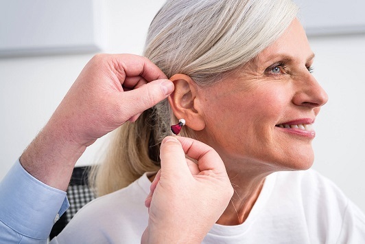 Frau lässt sich von einem Hörakustiker ein modernes Hörgerät ins Ohr einsetzen.